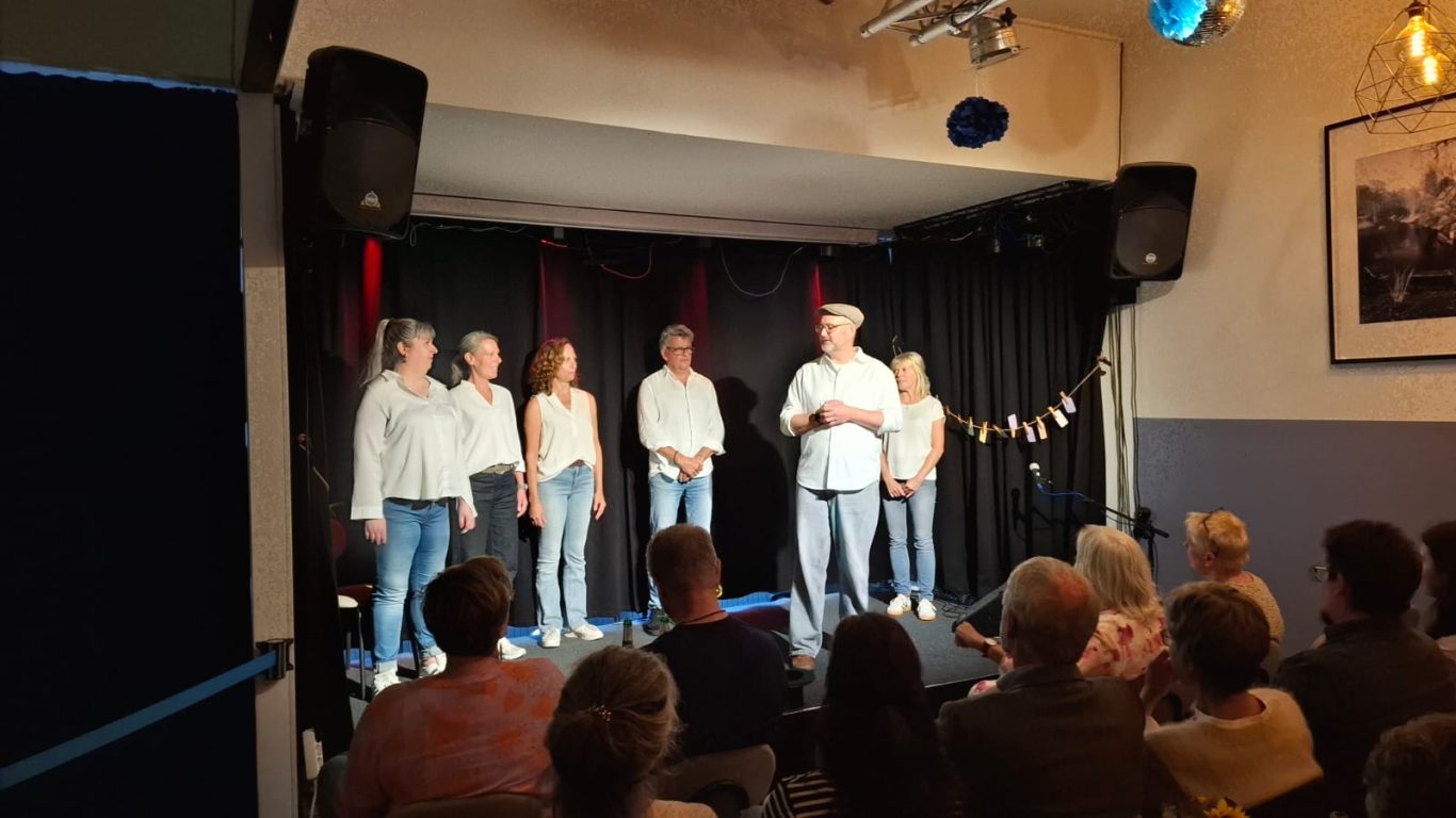 Spontanika auf der Kultavida-Bühne Mehrere Personen der Gruppe Spontanika stehen in hellen Oberteilen auf einer kleinen Bühne vor sitzendem Publikum.