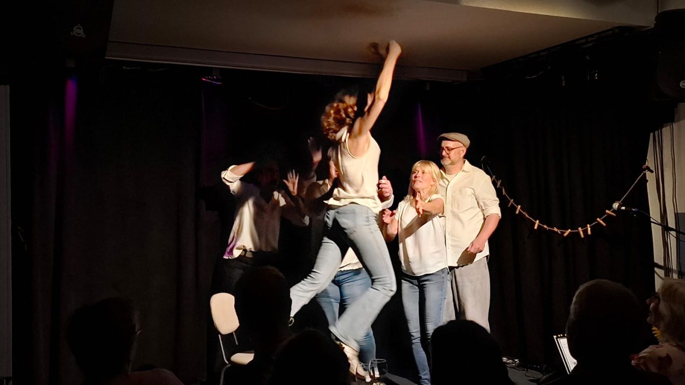 Das Finale von Inges Geschichte | Spontanika Eine Schauspielerin steht erhöht, während eine andere zu ihr aufblickt – das emotionale Ende einer Lebensgeschichte auf der Bühne.