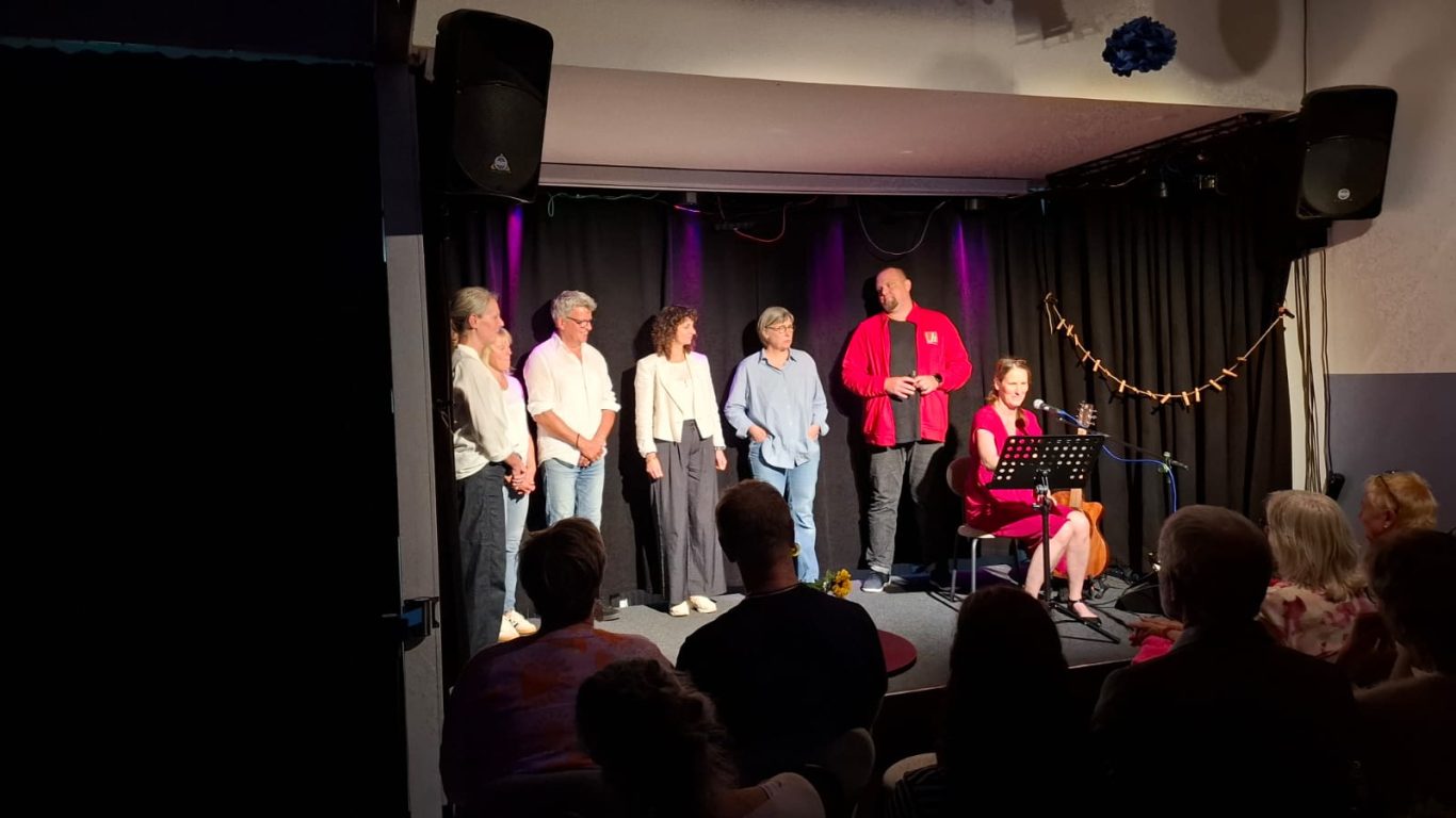 Gemeinsames Singen mit dem Publikum | Spontanika in Stormarn Spontanika, Stephanie Arndt und das Team stehen auf der Bühne und singen gemeinsam mit dem Publikum.