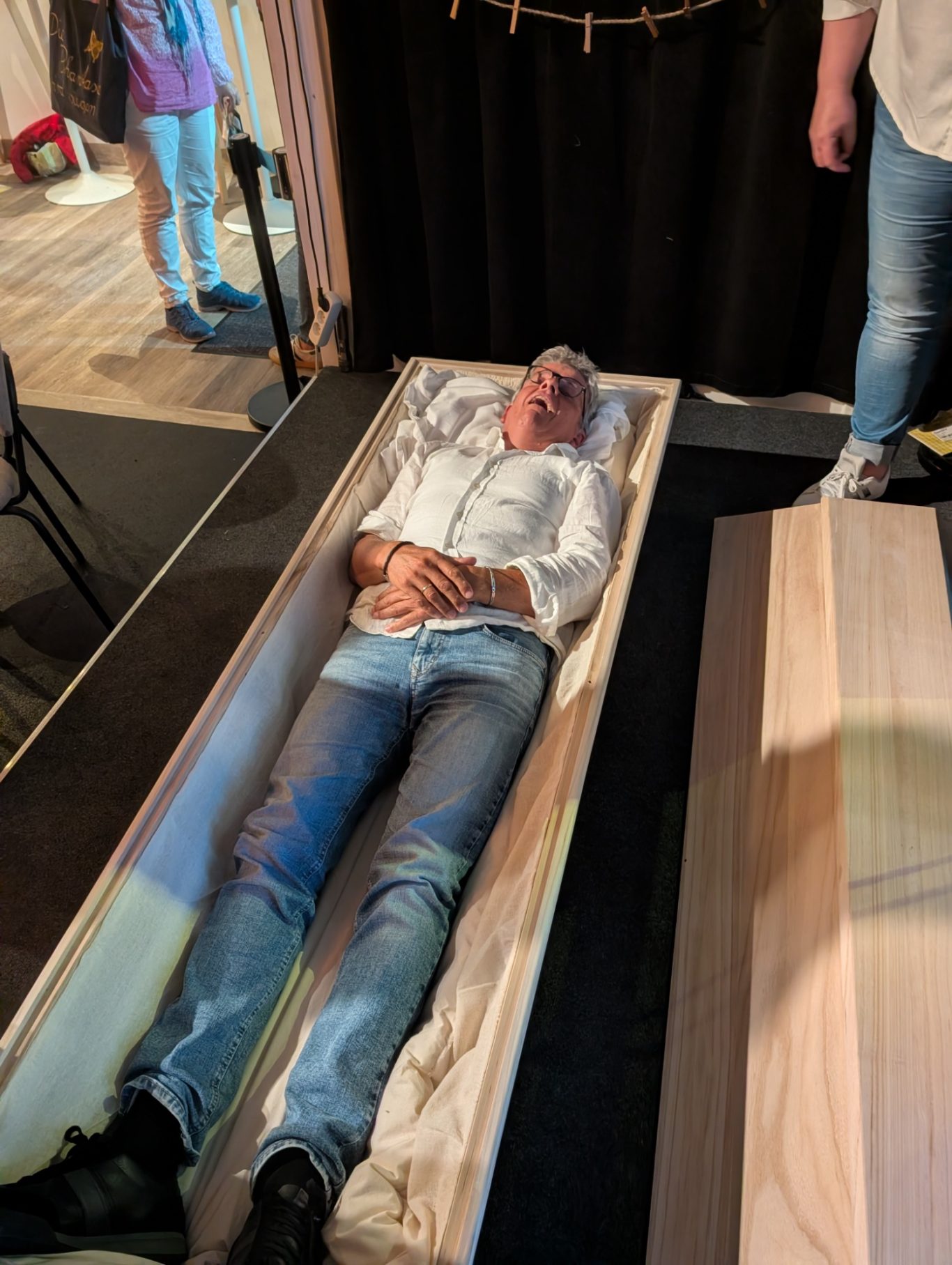 Sarg-Probeliegen | Improtheater Spontanika in Stormarn Ein Spontanika-Darsteller liegt im Holzsarg auf der Bühne und streckt scherzhaft grinsend die Hände nach oben.