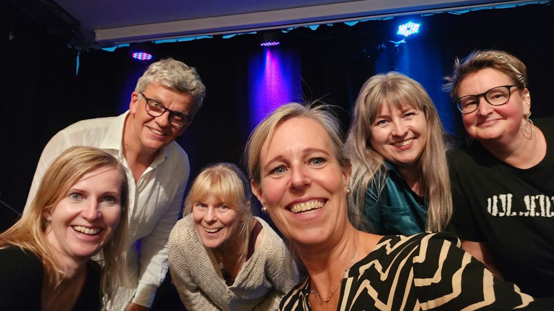 Ein gelungener Abend! Ein Selfie von einer sechsköpfigen Gruppe (fünf Frauen, ein Mann) mit glücklichen Gesichtern vor einer beleuchteten Bühne.
