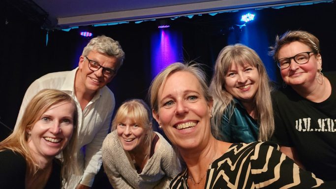 Ein gelungener Abend! Ein Selfie von einer sechsköpfigen Gruppe (fünf Frauen, ein Mann) mit glücklichen Gesichtern vor einer beleuchteten Bühne.