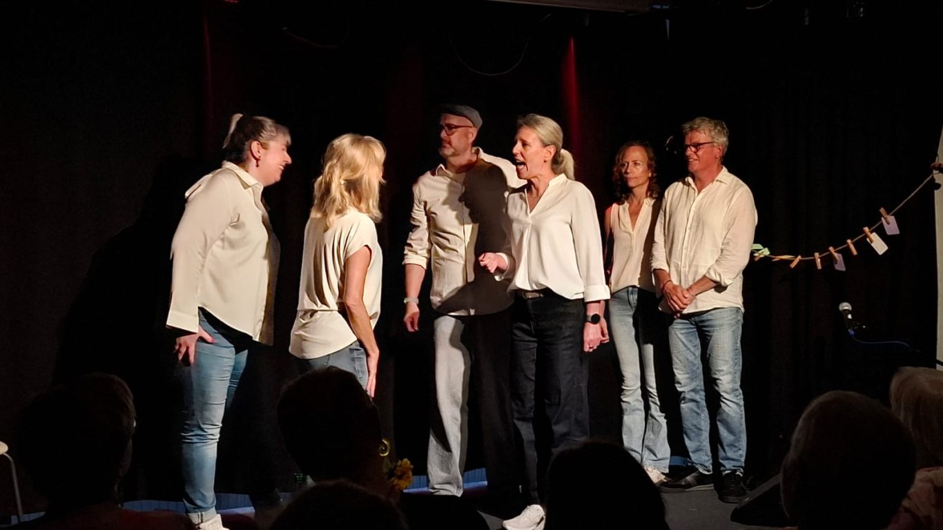 Szenenausschnitt von Spontanika Sechs Personen der Improgruppe Spontanika agieren dynamisch in einer Szene auf der dunklen Bühne.