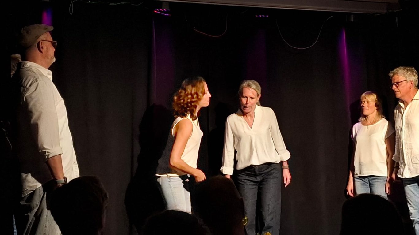 Dynamische Spontanika-Szene Eine Schauspielerin auf der Bühne gestikuliert dynamisch vor drei weiteren Ensemble-Mitgliedern.