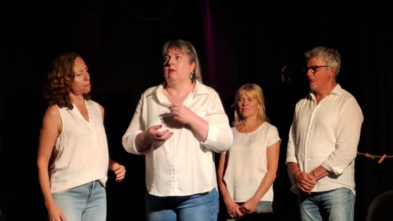 Fokussierte Szene auf der Bühne Vier Ensemble-Mitglieder von Spontanika stehen nebeneinander auf der Bühne, während eine Schauspielerin konzentriert spricht.