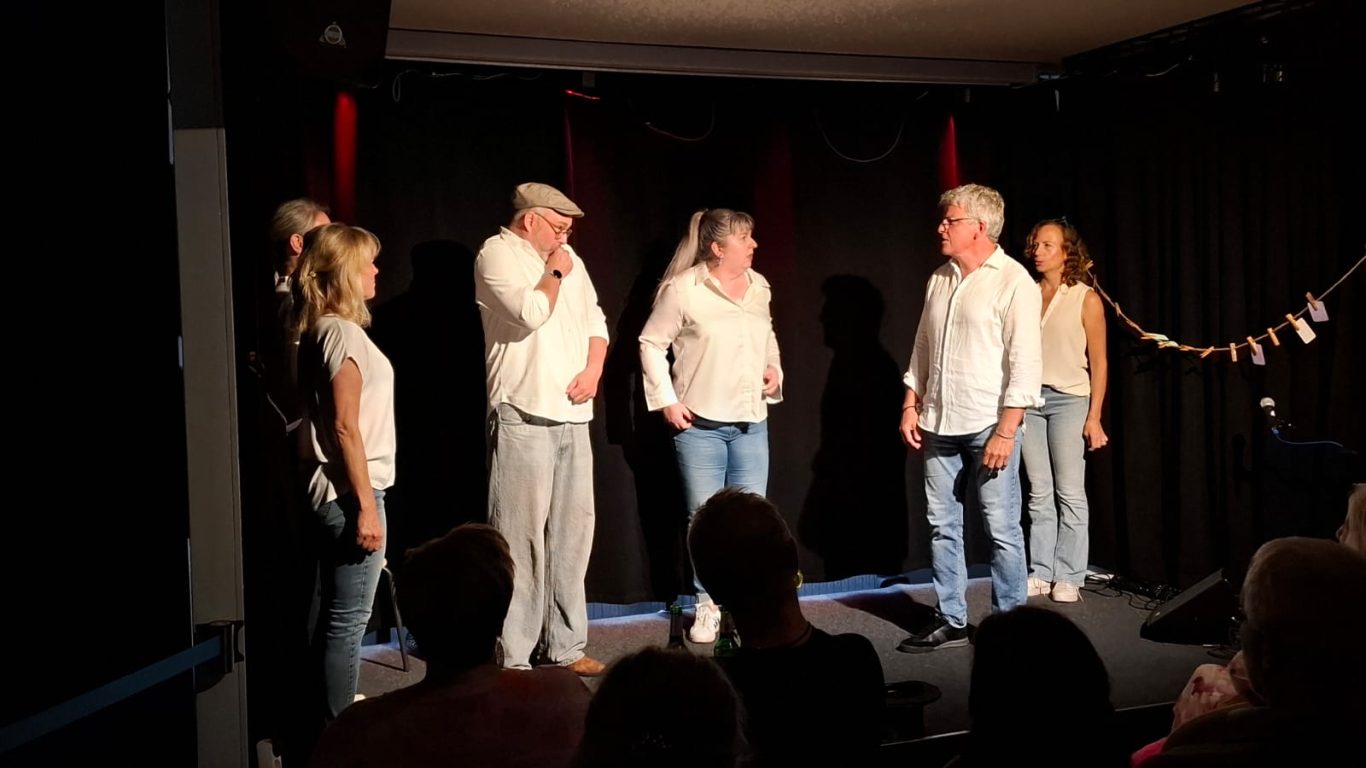 Szenenausschnitt von Spontanika Sechs Personen der Improgruppe Spontanika agieren dynamisch in einer Szene auf der dunklen Bühne.