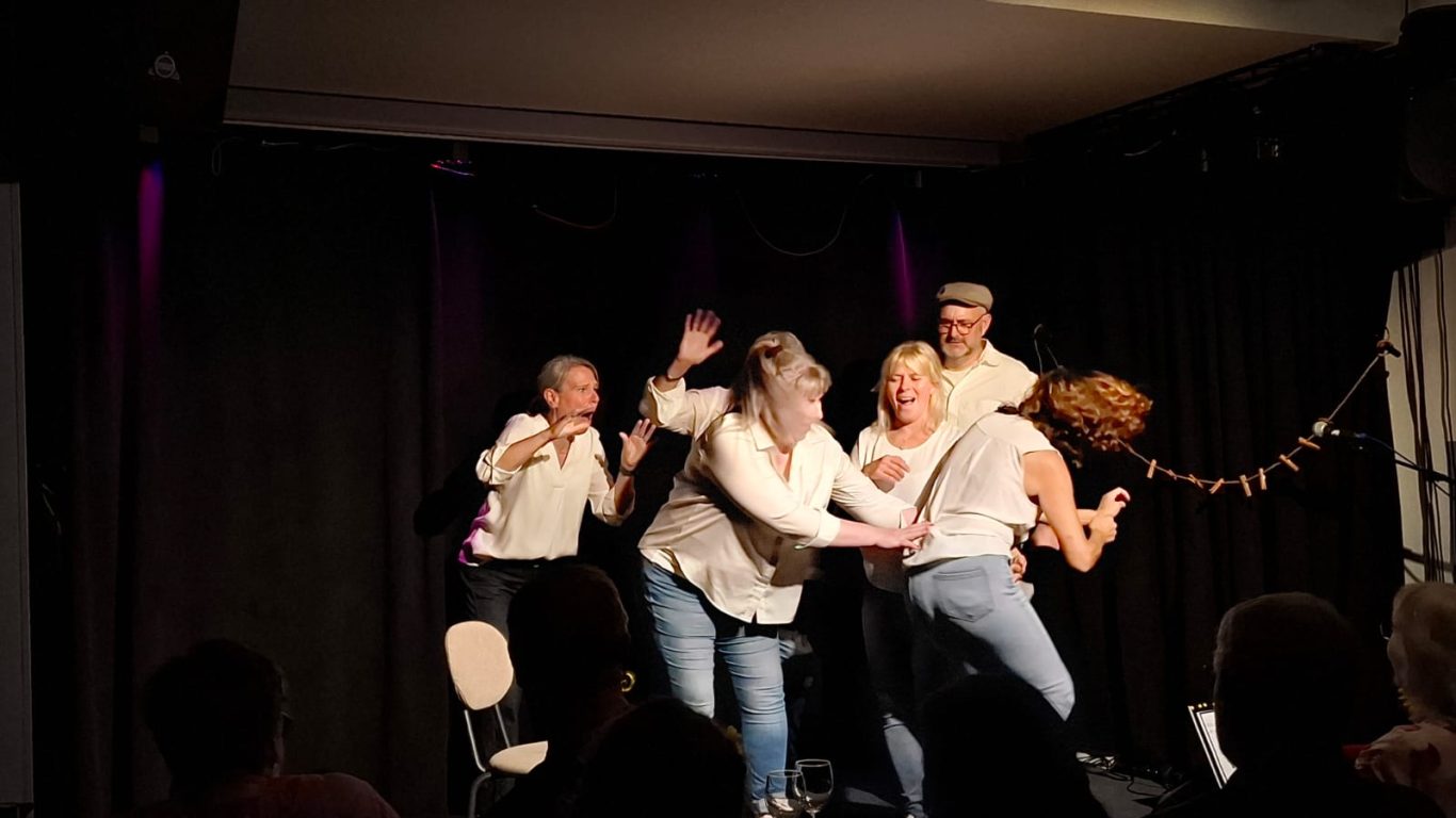 Das Finale von Inges Geschichte | Spontanika Eine Schauspielerin steht erhöht, während eine andere zu ihr aufblickt – das emotionale Ende einer Lebensgeschichte auf der Bühne.