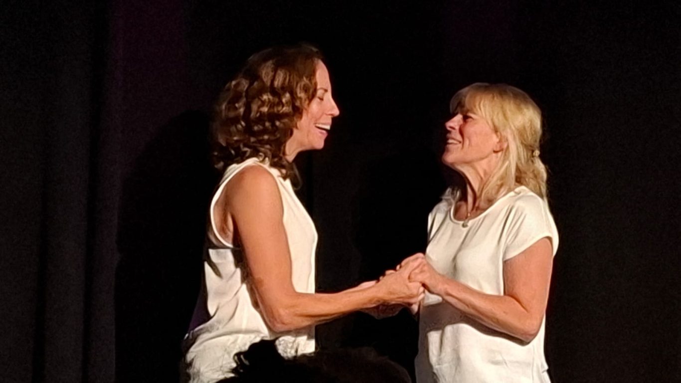 Inniger Bühnenmoment bei Spontanika Zwei Schauspielerinnen halten sich lächelnd an den Händen und blicken sich auf der Bühne an.