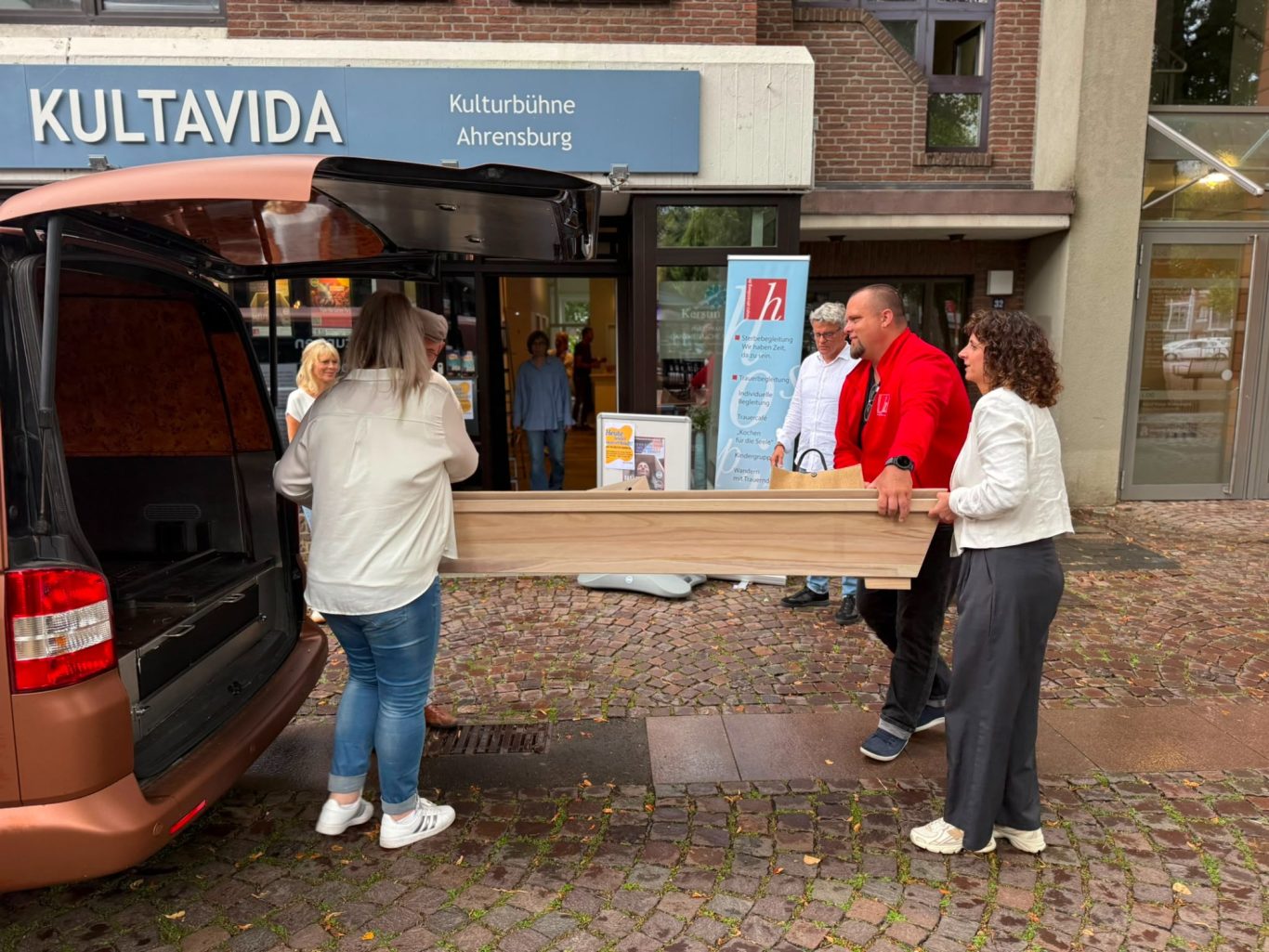 Sarglieferung für „Das letzte Lachen“ vor dem Kultavida Mehrere Personen tragen gemeinsam einen Sarg aus dem Kofferraum eines Autos vor dem Eingang der Kulturbühne Kultavida in Ahrensburg