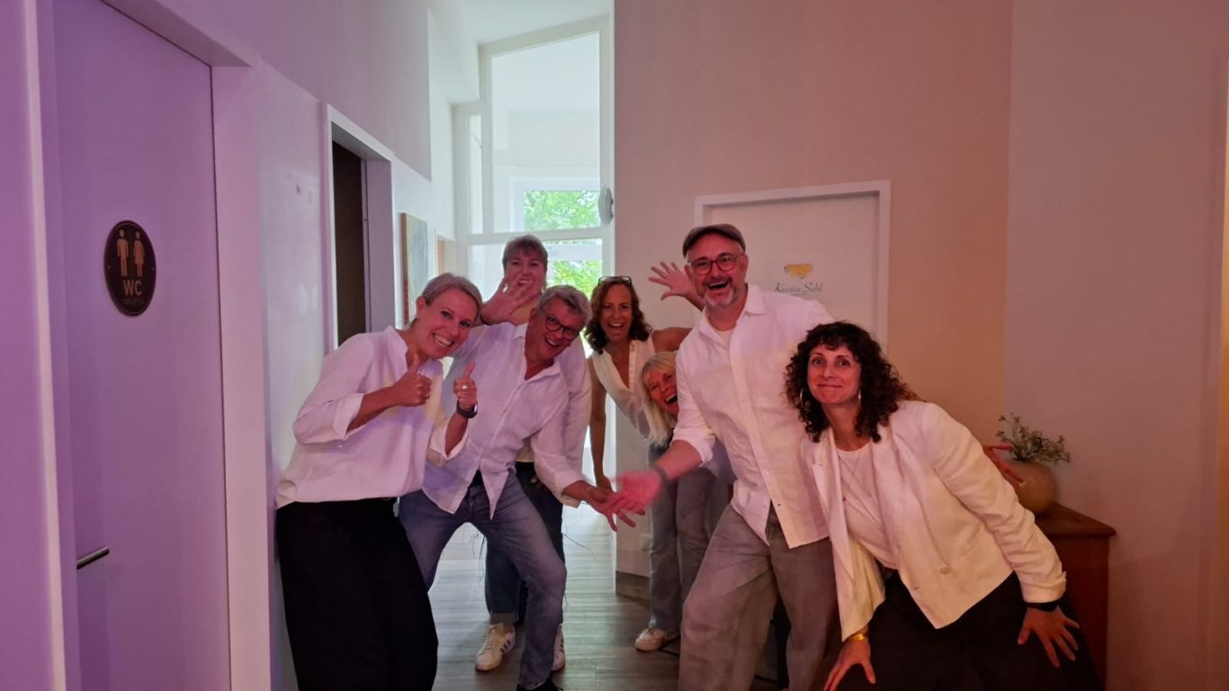 Spontanika und Esra (Bestattungsinstitut Lichtermeer) Die Gruppe Spontanika posiert gemeinsam mit Esra in hellen Oberteilen fröhlich im Flur des Kultavida.