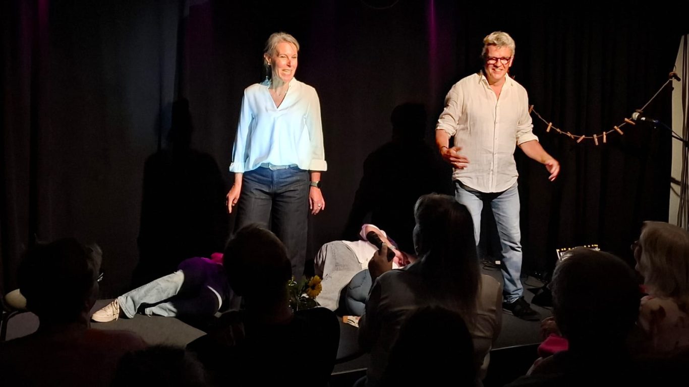 Impro-Game „Stirb!“ | Spontanika in Stormarn Spontanika-Darstellerinnen stehen auf der Bühne, während eine Person am Boden liegt – eine Szene aus dem Impro-Game „Stirb!“.